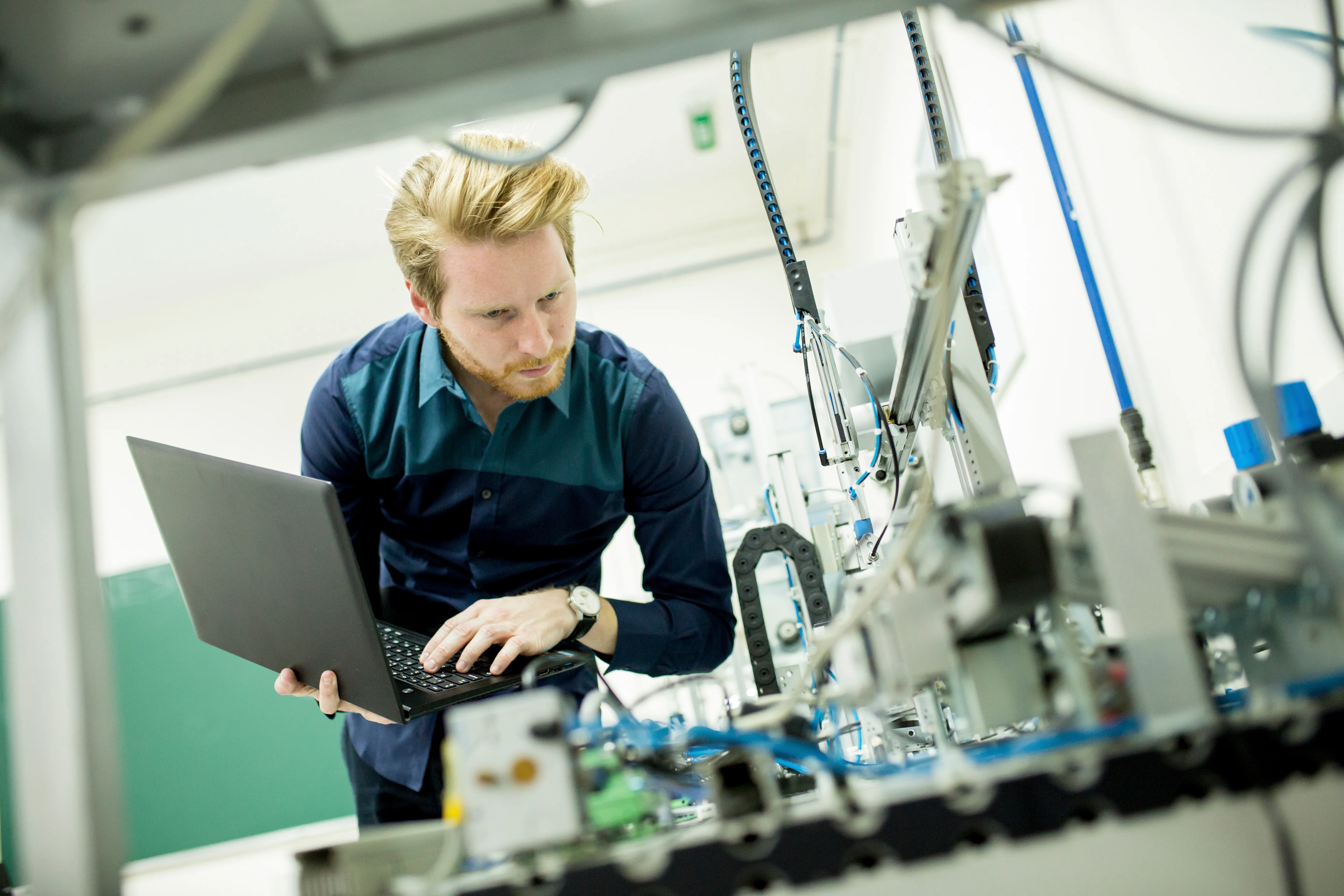 Engineer monitoring automated manufacturing equipment with a laptop